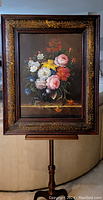 Framed painting displayed upright on wooden stand showing full composition