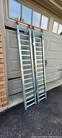 Two aluminum loading ramps standing vertically against a garage door, showing full length and height.