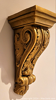 Side view of a gold decorative wall bracket showing detailed scrollwork and leaf motifs