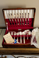 Opened wooden box displaying a full set of silver plated flatware with red velvet interior lining