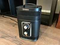 Black Westinghouse 360 degree ceramic space heater with two control knobs on front, placed on a wooden floor.