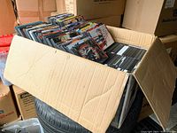 Large cardboard box with DVDs arranged vertically showing colorful DVD covers inside a storage area with other moving boxes.