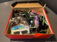 Box of various sunglasses and eyeglasses in assorted colors and styles, some packaged, some loose.