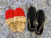 Top view of a pair of red women's slippers with knit texture and faux fur trim alongside a pair of black men's moccasin slippers, both new.