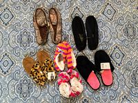 Top view of six pairs of slippers and two pairs of girls' slipper socks on a patterned fabric surface.