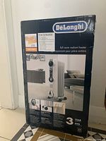 Front view of boxed DeLonghi full room radiant heater showing product image, brand, wattage, 3 year warranty badge, and product details.