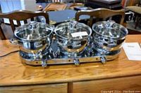 Ronco triple burner hot plate with three matching stainless steel pots with glass lids on a wooden surface