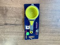 Silicone tea strainer in bright green attached to blue branded cardboard backing indicating it is new and designed to pass tea in seconds.