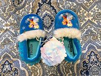 Top view of blue toddler slippers showing Frozen characters Anna and Elsa with white furry lining and attached tags.
