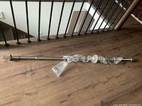 Single metallic weightlifting barbell laid horizontally on wood floor, partially wrapped in protective plastic covering.