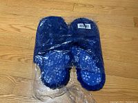 Top view of the blue slippers with white snowflake patterns in original plastic wrapping showing front design.