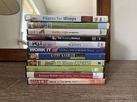 Pile of 11 workout DVDs, titles readable on spines, showing variety of fitness programs including yoga, pilates, seniors, walking workouts.
