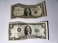 Two U.S. paper bills laid flat; top $1 Silver Certificate, bottom $2 bill