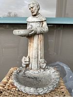 Full front view of concrete bird feeder sculpture showing robed man holding bowl over a larger basin with two birds at feet.