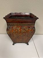 Front view of the embossed metal planter showing the ornate floral embossing and scalloped rim.