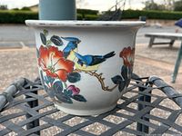 Front view showing two blue and yellow birds perched on a branch with red flowers painted on the ceramic garden pot.