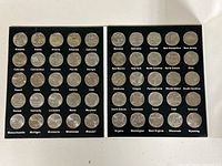 Top view of two black panels holding fifty US state quarters, each coin labeled with a state name in white lettering.