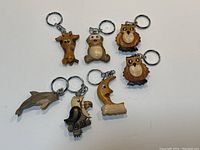 Seven wooden animal keychains arranged on white background. Items are a giraffe, bear, two owls, dolphin, dog, and crescent moon face.