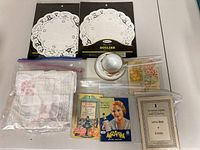 Wide shot showing all items: two packs of paper doilies, cloth doilies, three dessert cookbooks, and a tea cup with saucer.