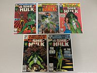 Five She-Hulk comic books laid out in two rows showing colorful covers and titles