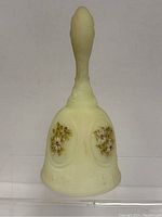 Side view of opaque yellow glass bell with floral accents on bell body and handle with leaf detail