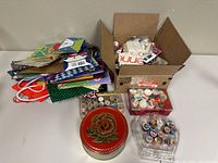 Wide view of whole lot showing gift bags stacked on side, cardboard boxes and round decorative tin with sewing supplies inside