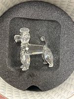 Top-down view of Swarovski crystal poodle lying in black foam in round box.