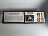 Open black presentation portfolio showing the left side panel with historic and descriptive text about the proof silver dollar coin and First Day Issue stamp set titled 'The Cornerstones of Freedom'.