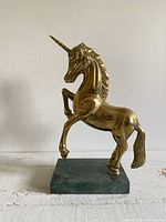 Front-side view of the brass unicorn rearing on green stone base, showing polished brass surface and detailed sculpting.