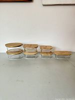 Full view of all 8 mixed glass storage containers with bamboo lids in varying sizes, aligned in rows.