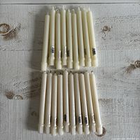 Top view of two groups of white wax taper candles arranged on a wooden surface, showing differences in size and base design.