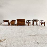 Full set of seven miniature wooden dollhouse furniture items arranged in a row against a white wall on textured surface.