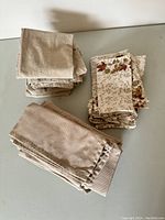 Three distinct stacks of fabric napkins on a gray surface showing neutral tones and patterns including solid beige, floral print, and tan striped.