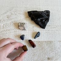 Photo showing six stones including one large rough black stone, one white with black matrix, and four polished smaller stones.