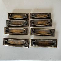 Top-down view of eight reclaimed metal dresser drawer handles with visible patina and wear.