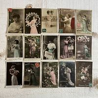 Set of fifteen vintage French postcards depicting women in period attire, some colorized, with various floral and letter themes, arranged on fabric background.
