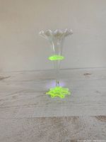 Full view of the clear Vaseline uranium glass vase with a ruffled flared rim and star-shaped stretched base glowing under UV light, showing its distinctive green fluorescence.