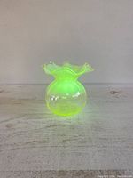 Photo of small Vaseline uranium glass vase glowing bright green under UV light, showing its fluorescent property.
