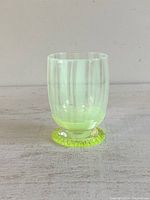 Front view of the glass cup showing clear body with vertical striped detailing and yellow-green glowing decorative base