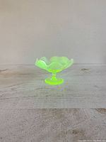 Front view of Victorian Vaseline uranium glass dish with glowing green color under light, showing frilled rim.