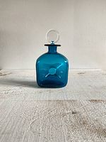 Front view of blue glass decanter with clear stopper on top, showing bubble detail on front face.