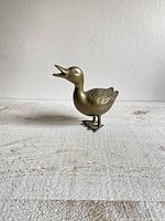 Side view of brass duck figurine showing open bill and detailed wings.