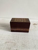 Front view of the rectangular wooden box displaying carved decorative design on the lid and side with geometric patterns.