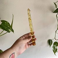 Hand holding clear tapered Lucite candle with gold foil flakes visible inside, against a plain wall.