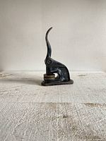 Side view of vintage black metal embossing press with curved handle resting on a textured white surface.