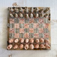 Top-down view of the stone chess board set up with full pieces in two colors pink and gray marble tones.