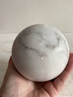 Close-up of the marble sphere being held, showing polished white marble with gray veining.