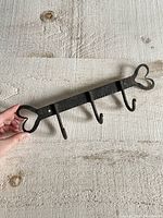 Full view of vintage metal rack held in hand, showing three hooks and heart-shaped ends.