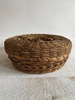 Side view of round woven wicker basket with lid showing braided details and woven texture.