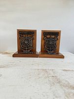 Pair of vintage wooden bookends with metal Queen's University crests side by side on white table.